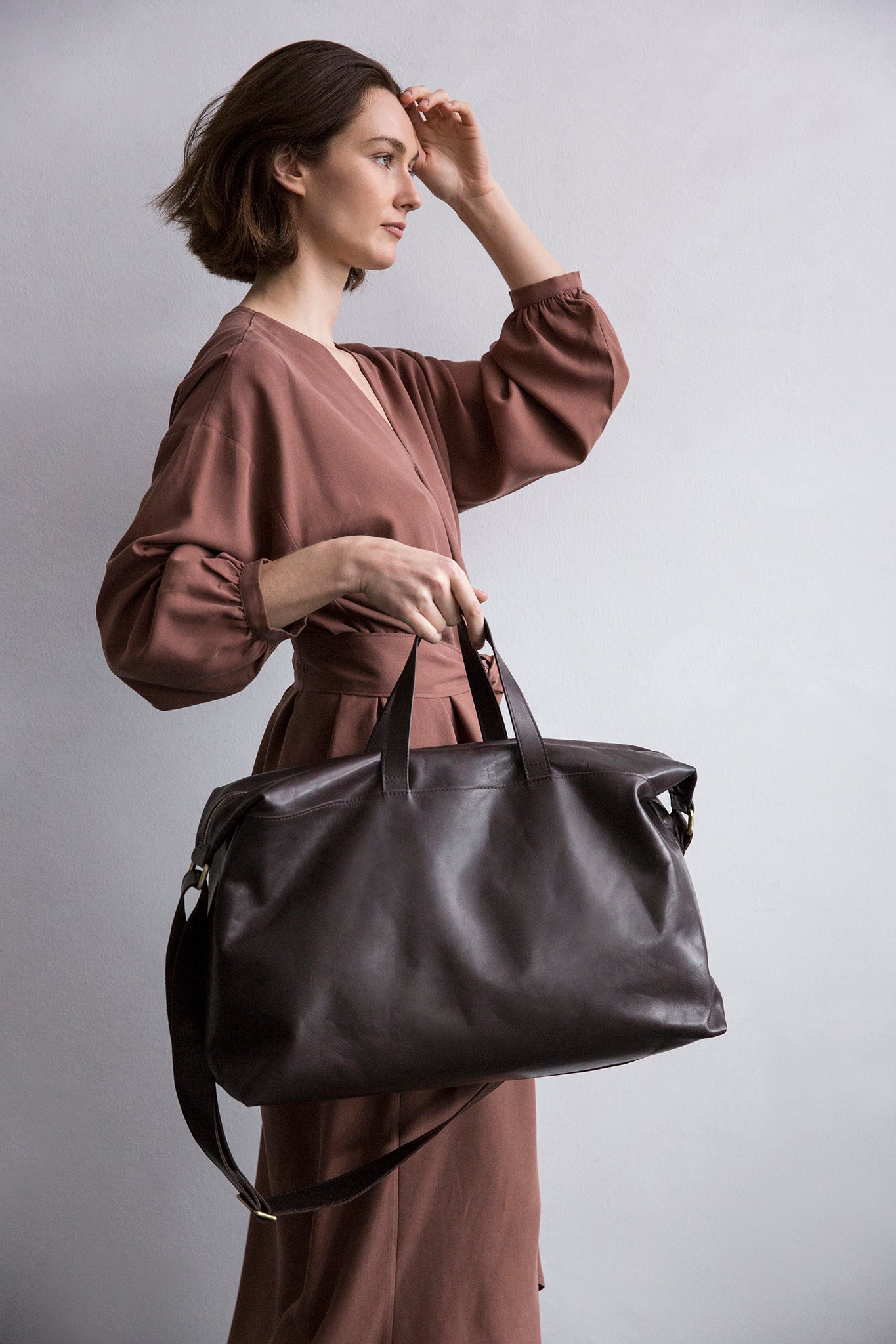 Cognac leather weekender worn on the shoulder, minimalist design.